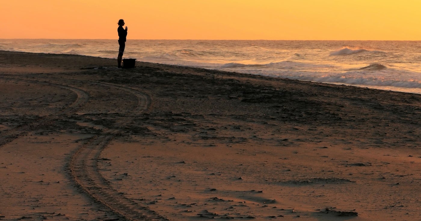 Person meditating on beach at sunrise