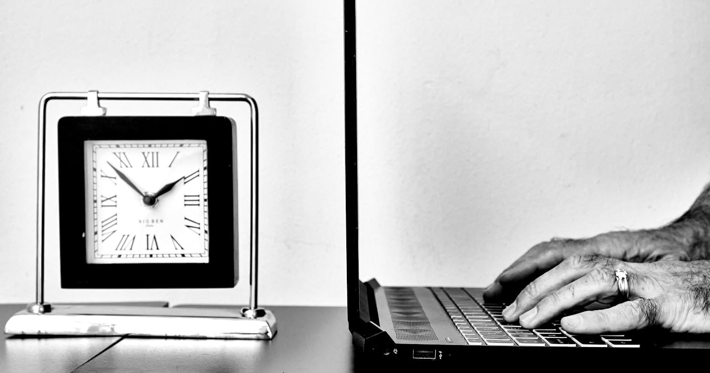 Person typing on a laptop next to a timer clock, using the Pomodoro Technique for focused work